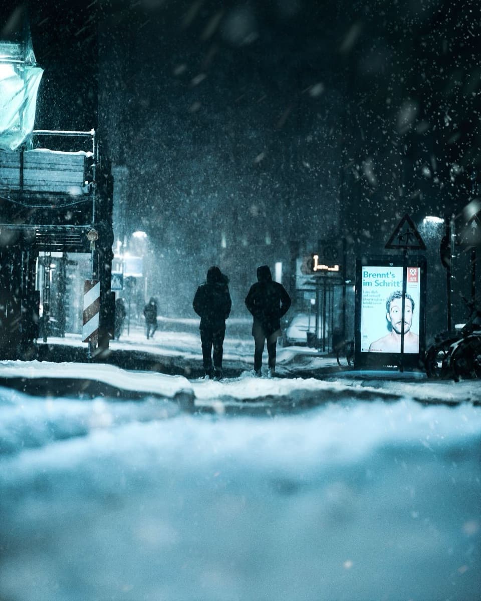 Zwei Menschen gehen im Schneefall eine Straße entlang